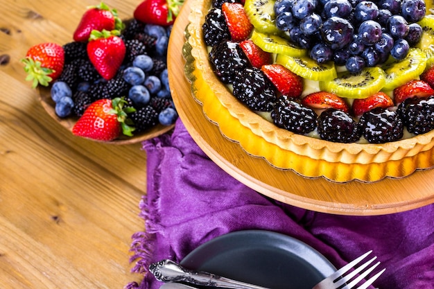 Пирог со свежими фруктами на подставке для торта на деревянном столе.