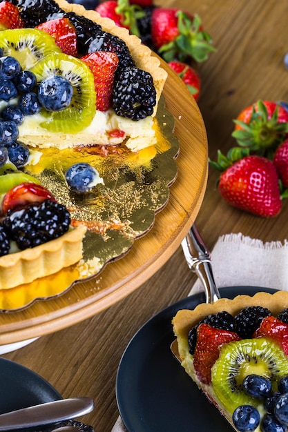 Photo fresh fruit tart on cake stand on wood table.