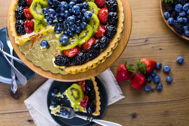 Фото Пирог со свежими фруктами на подставке для торта на деревянном столе.