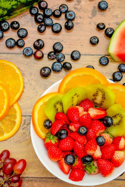 신선한 과일 개념 열대 과일과 나무 배경에 있는 그릇에 모듬 베리 샐러드