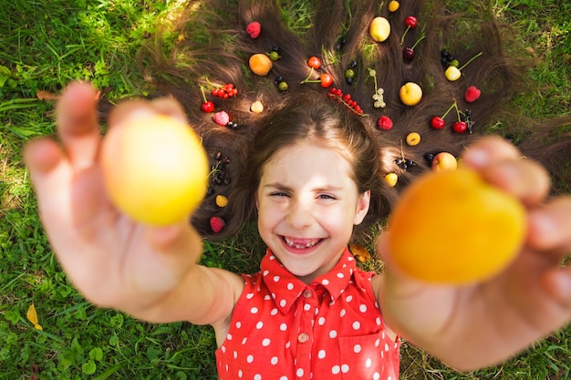 Fresh fruits, healthy food concept - girl lay with fruits on her hair