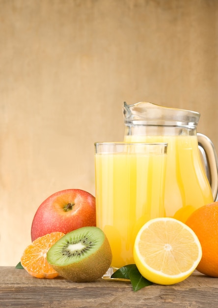 Fresh fruits juice in glass and slices on wood background