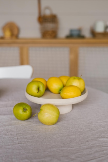 Fresh fruits lemons and green apples are on a white plate on the kitchen table