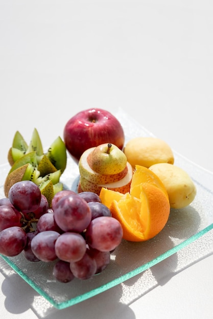 白いテーブルの上のプレートに新鮮な果物キウイグレープオレンジアップルスピアーズヘルシーダイエットとローカロリーダイエットヘルシーベジタリアンフードコピースペース