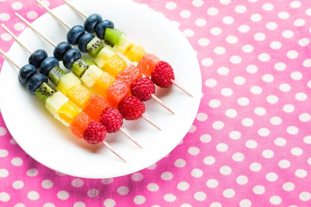 Fresh fruits on skewers in plate on table