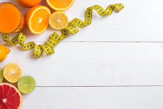 Fresh fruits with tape measure over white wooden background top view