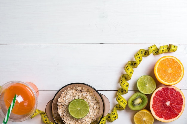 Fresh fruits with tape measure over white wooden background top view