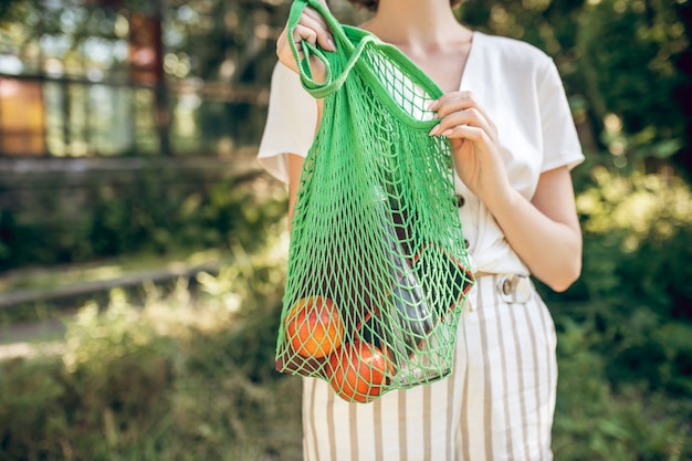 Photo fresh fruits. young girl with a green mesh bag with fruits in hands