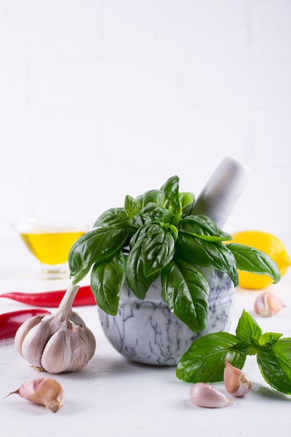 Fresh garden basil herbs in mortar and olive oil, garlic , red hot chili peppers, lemon on the white background.