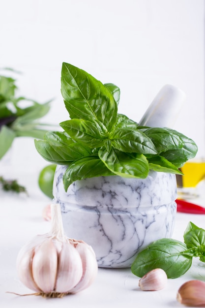 Photo fresh garden basil herbs in mortar and olive oil, garlic , red hot chili peppers, lemon on the white background.