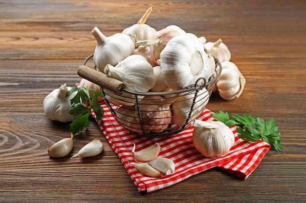 Fresh garlic in the basket decorated with parsley and red checkered cotton napkin on wooden background
