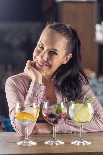 Fresh gin tonic cocktails with fruit and ice in front of a happy good-looking girl sitting on a bar.