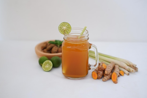 Fresh ginger and lemon juice in a glass jar with ginger roots on white background