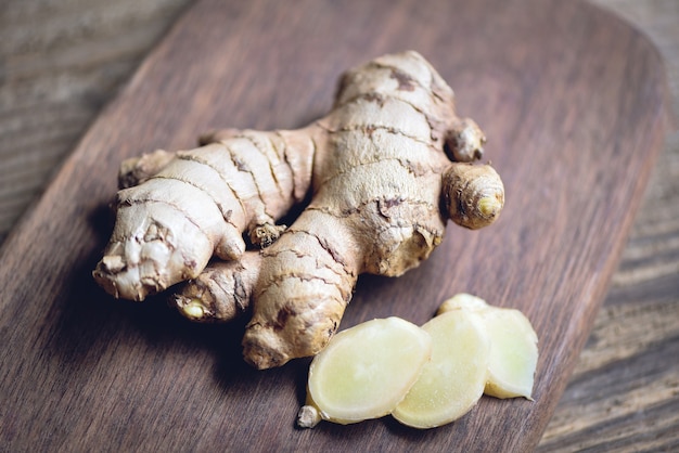 Fresh ginger root on cutting board with sliced ginger on wooden background