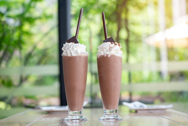 Foto un fresco bicchiere di latte ghiacciato cioccolato sopra panna montata cacao dolce ghiaccio in bel bicchiere dolce dolce già da bere su un vassoio di legno cioccolato fatto in casa per bambini