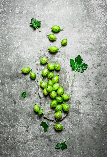 Fresh gooseberries with leaves on stone table.