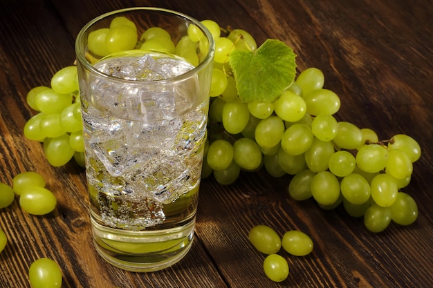 Fresh grape juice with ice cubes in glass and bunch of sweet green grape on wooden table.