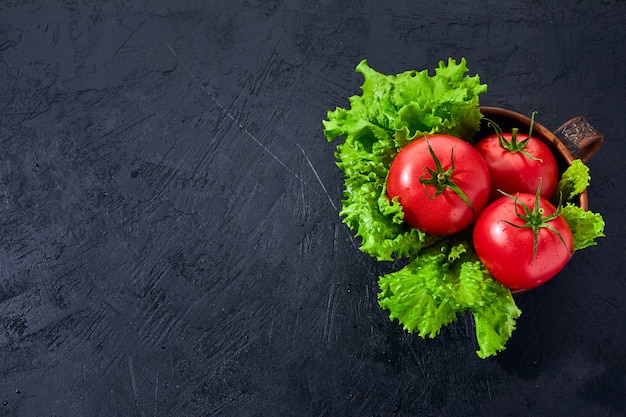 Pomodori d'uva freschi con foglie di insalata su fondo di pietra nera concetto di cottura dei pomodori alle erbe