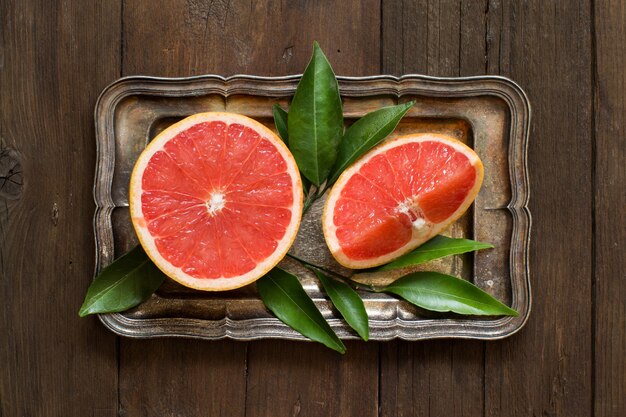 Photo fresh grapefruit with leaves  on a tray on a wooden table top view