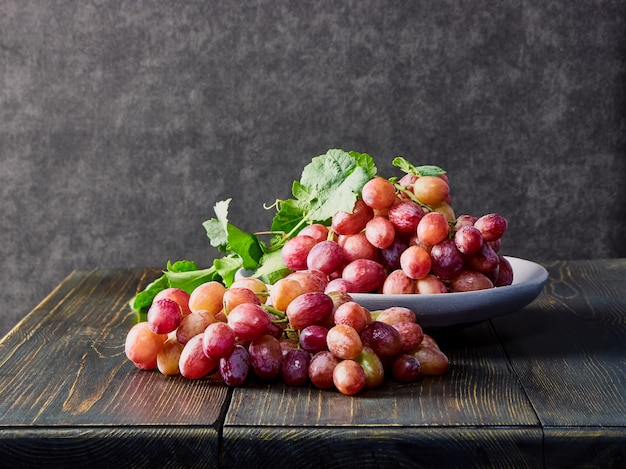 Fresh grapes. Bunches of different varieties in a plate on an old wooden table