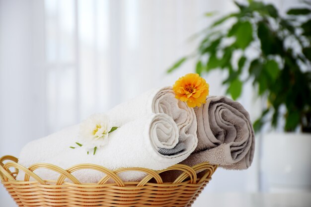 Fresh gray and white towels rolled in wicker bascket decorated with flowers and liquid container.