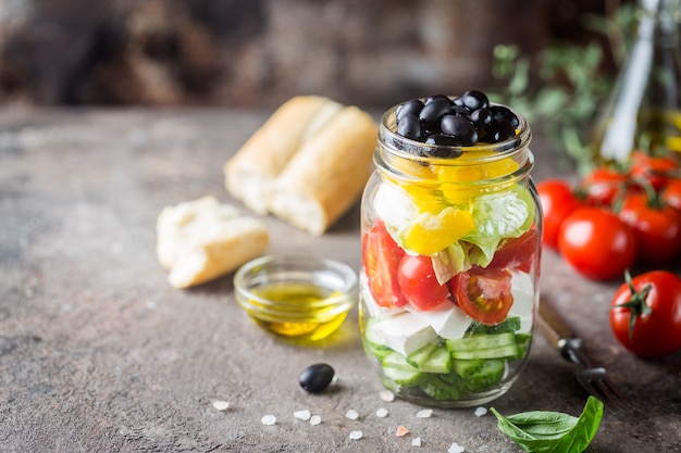 Свежий греческий салат из огурцов, помидоров, сладкого перца, сыра фета и оливок с оливковым маслом в стеклянной банке