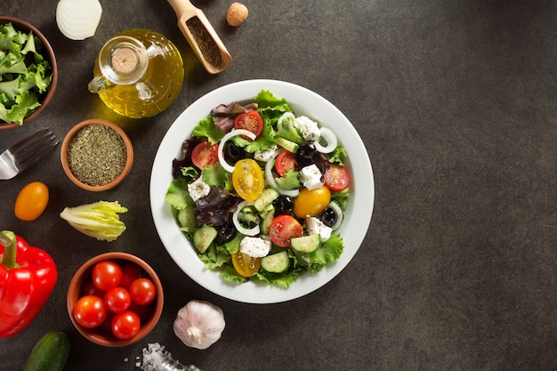 Fresh greek salad in plate and ingredients on stone table