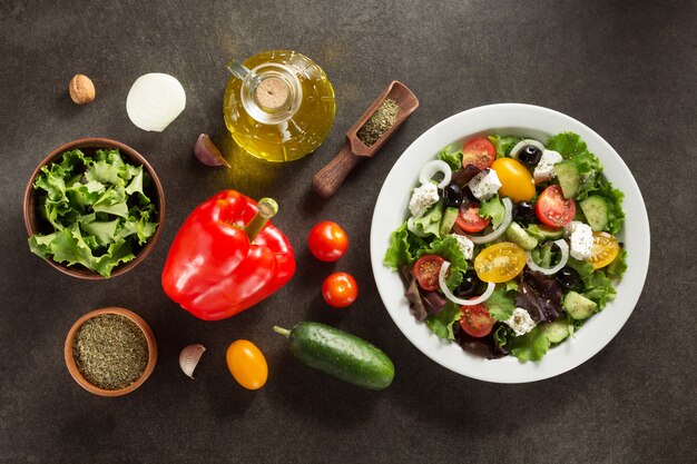 Fresh greek salad in plate and ingredients on stone table