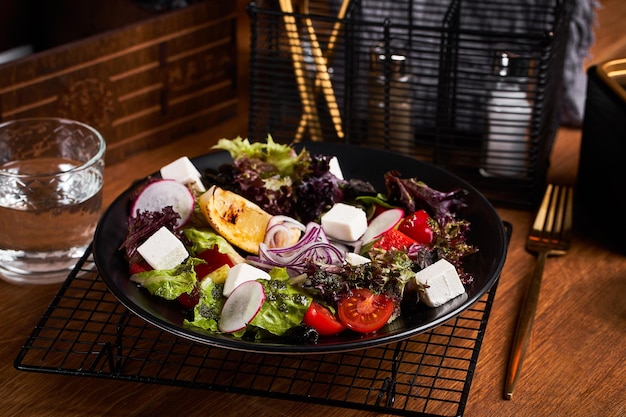 Fresh greek salad with tomato radish onion bel pepper olives and feta cheese on black plate side view wooden background