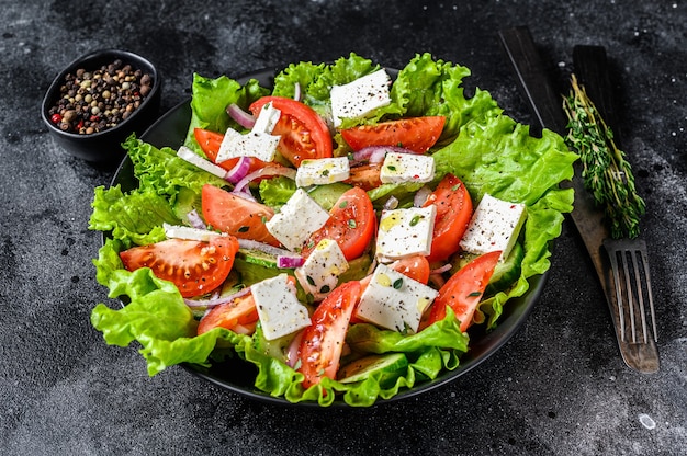 Fresh Greek salad with vegetables and feta cheese in a plate. Black table. Top view.