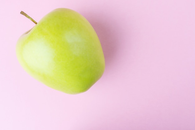 Fresh green apple on the background of a pastel pink wall. 