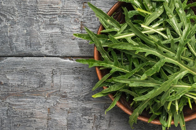 Foglie di rucola verde fresca in una ciotola su un tavolo di legno nero posa piatta