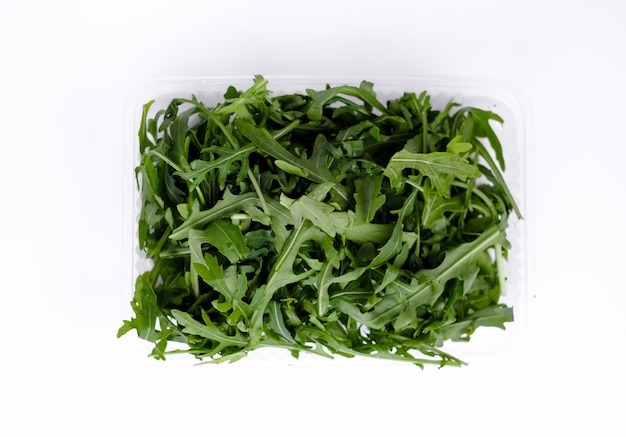 Fresh green arugula leaves at plastic container on white background