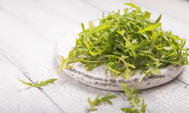 Fresh green arugula leaves on white board, rucola rocket salad on wooden rustic background with place for text. Selective focus,  healthy food, diet. Nutrition concept