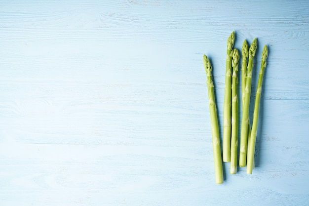 Fresh green asparagus on blue wooden surface, place for text. Top view.