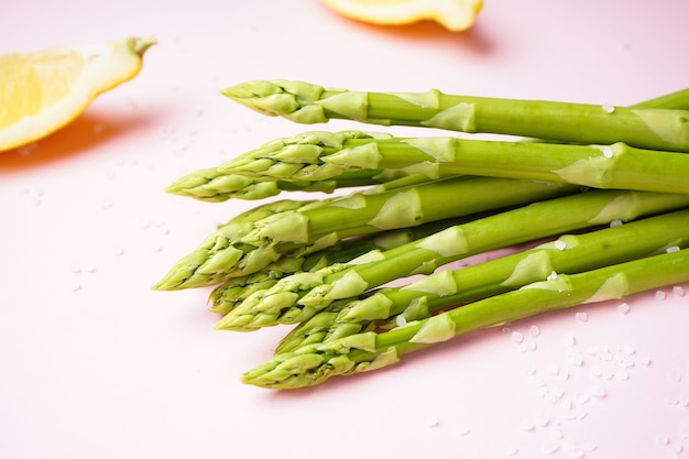 Fresh green asparagus and lemon wedges on pink surface. Close-up.