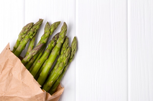 Fresh green asparagus in paper shopping bag on white wooden table table.