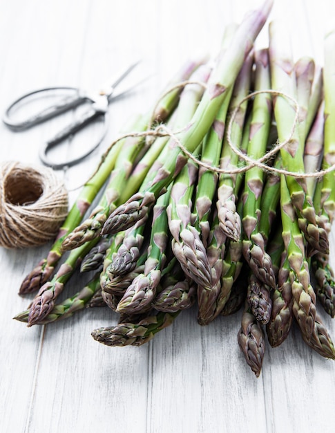 Fresh green asparagus with scissors and thread on old wooden table