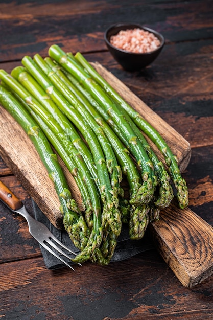 Fresh green asparagus on a wooden cutting board. Dark wooden background. Top view.
