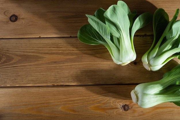 Fresh green bok choy or pac choi chinese cabbage on a brown wooden background. Hard light, contrast. Top view, copy space, flat lay.