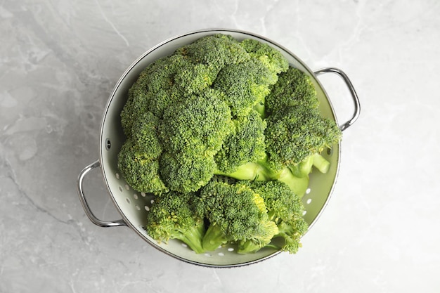 Fresh green broccoli in colander on grey marble table top view