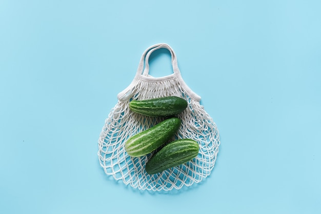 Fresh green cucumbers vegetables on reusable shopping eco-frendly mesh bag on blue background