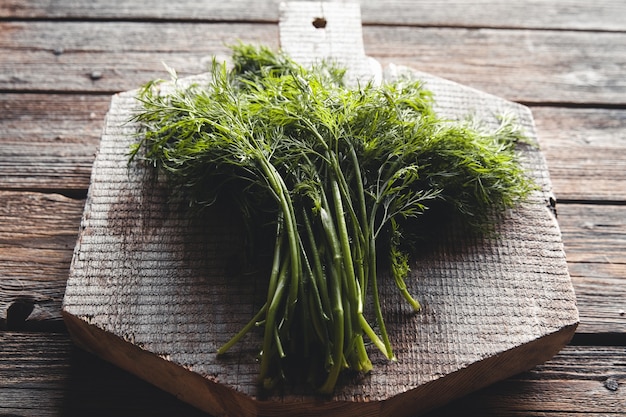 Fresh green dill on the wooden cutting board closeup. Fresh herbal condiment dill for cooking.