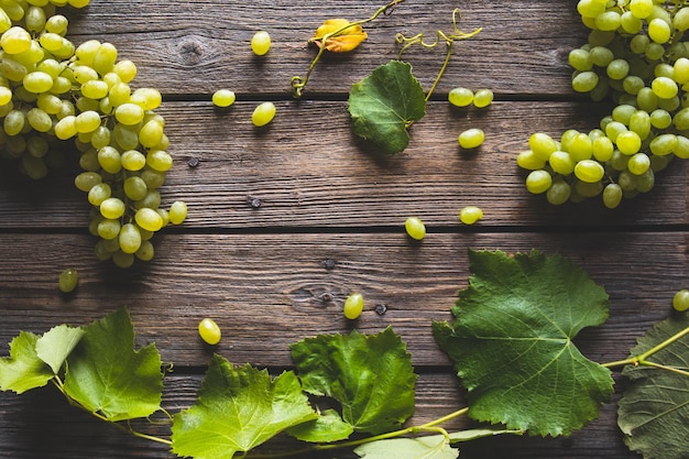 Uva verde fresca con foglie su fondo in legno