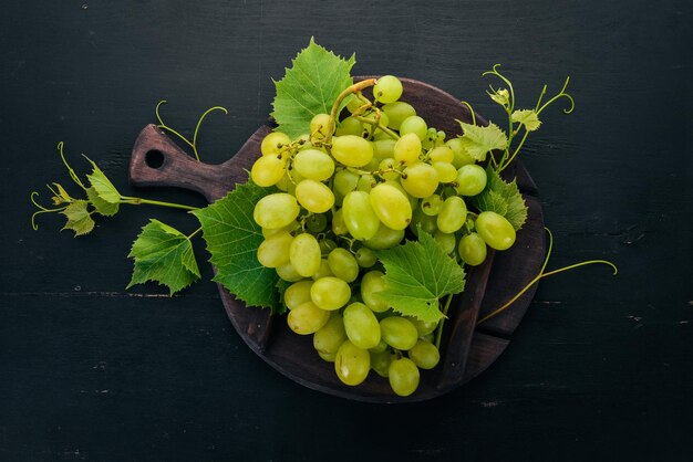 Fresh green grapes with leaves of grapes Top view On a black wooden background Free space for text