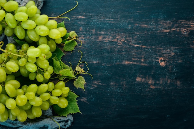 Fresh green grapes with leaves of grapes Top view On a black wooden background Free space for text