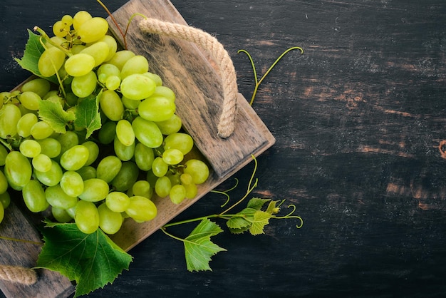 Fresh green grapes with leaves of grapes Top view On a black wooden background Free space for text