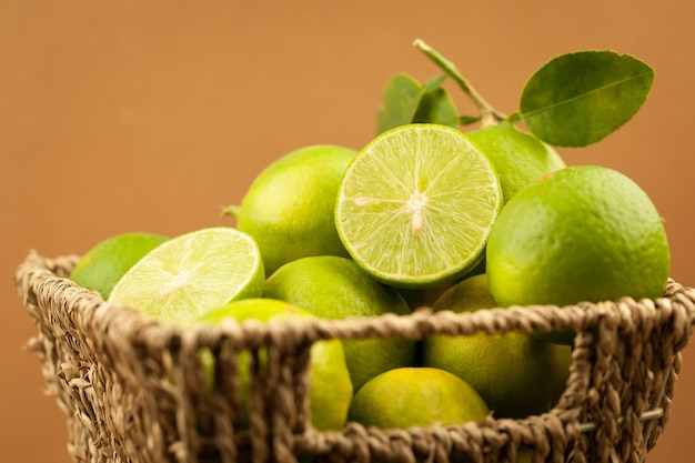 Fresh green lemon with green leaves in basket on brown