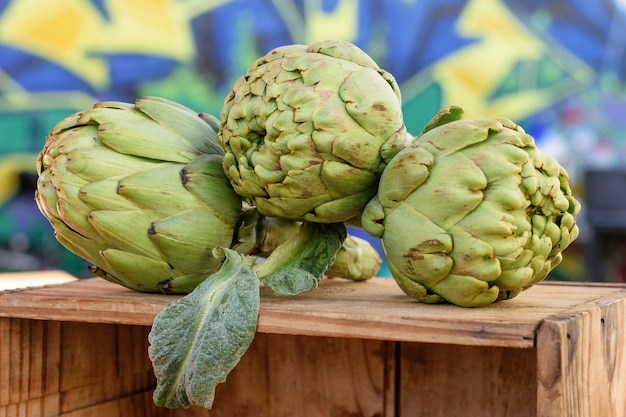 Fresh green mediterranean artichokes on the wooden box for sale one holiday at the market.