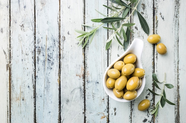 Fresh green olives in a bowl and olive branch on rustic wooden